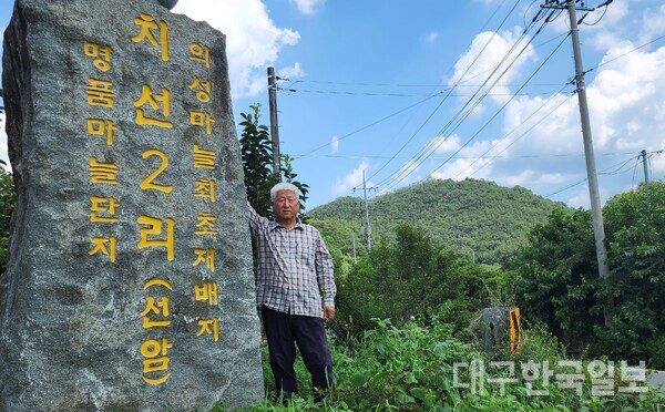 손윤동씨가 의성 마늘 최초 재배지 표지석 옆에 서서 기념 촬영을 하고 있다.